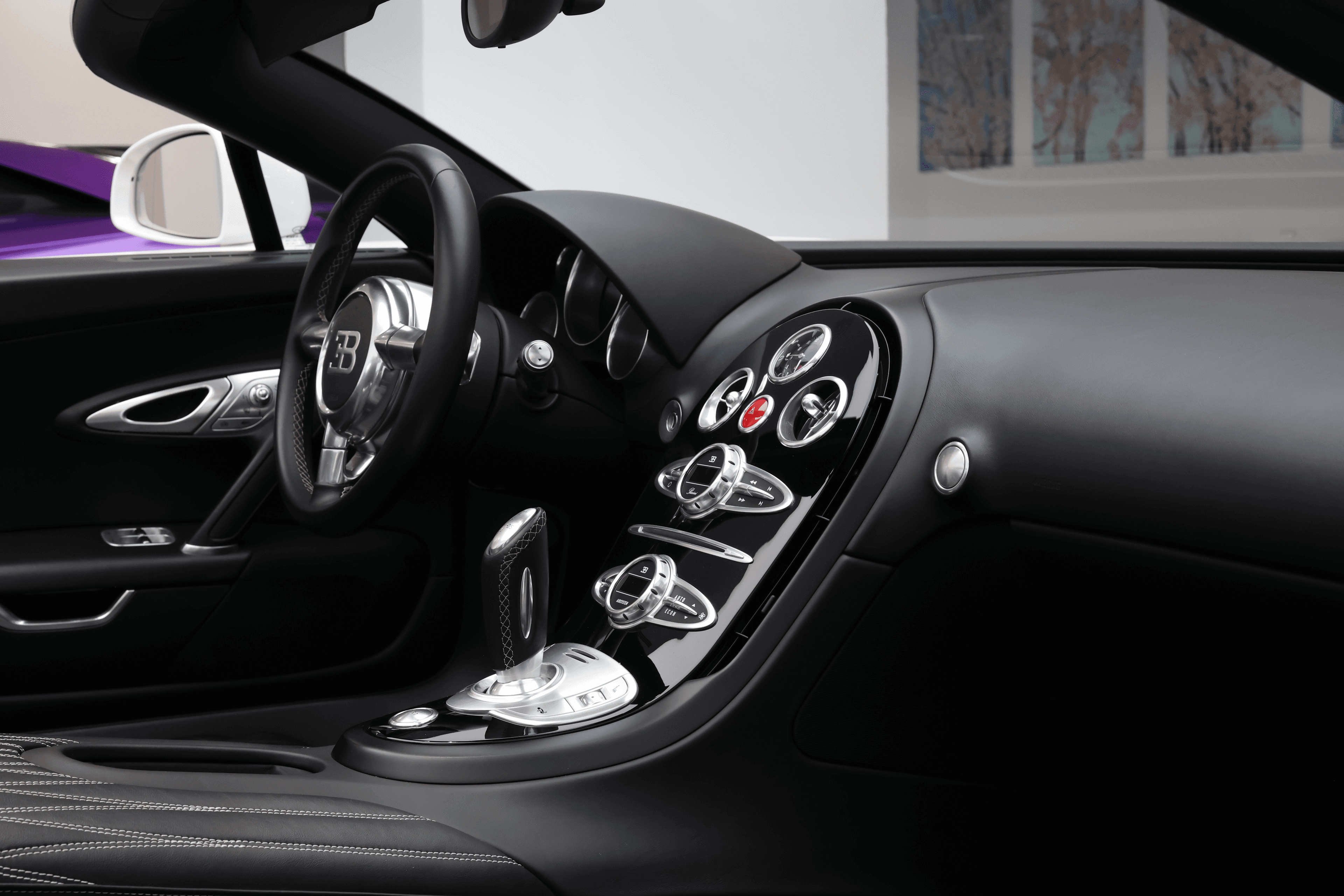 Du côté passager, l'intérieur de la Bugatti Veyron se dévoile avec un cuir de haute qualité, des finitions impeccables et une ambiance luxueuse, offrant une vue sur le tableau de bord et le volant qui évoquent la performance et le raffinement.