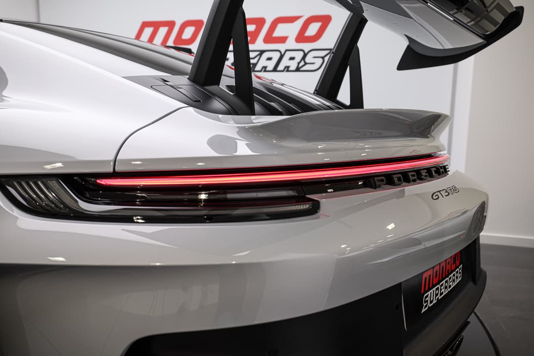 L'image présente l'arrière d'une Porsche 911 GT3RS gris glacé, mettant en valeur son aileron distinctif et le logo "Porsche" 