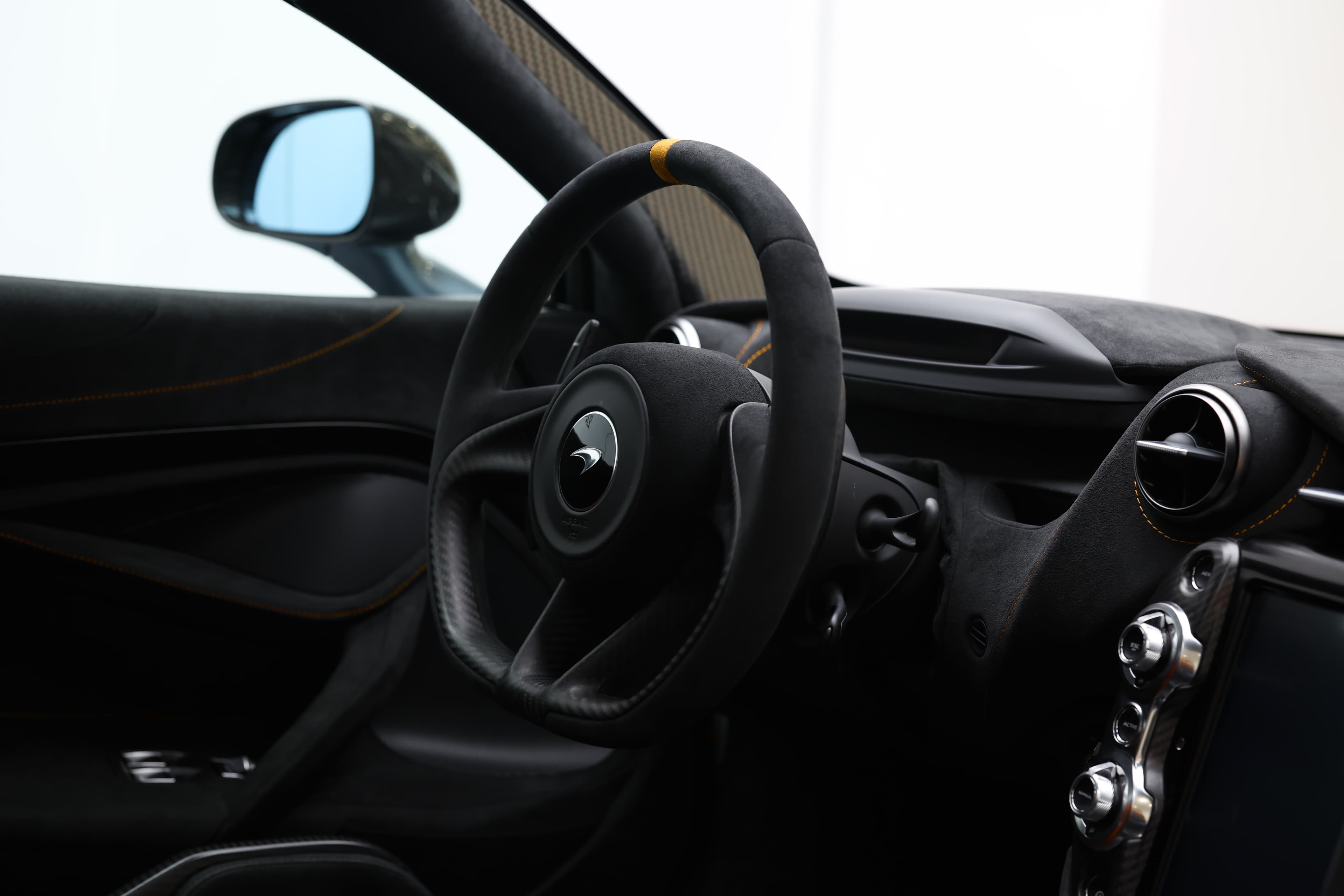 L'image montre l'intérieur de la McLaren 765LT, en mettant l'accent sur le volant, qui présente un design sportif et ergonomique, avec des commandes intégrées et des matériaux haut de gamme, reflétant l'attention portée aux détails et à la performance.