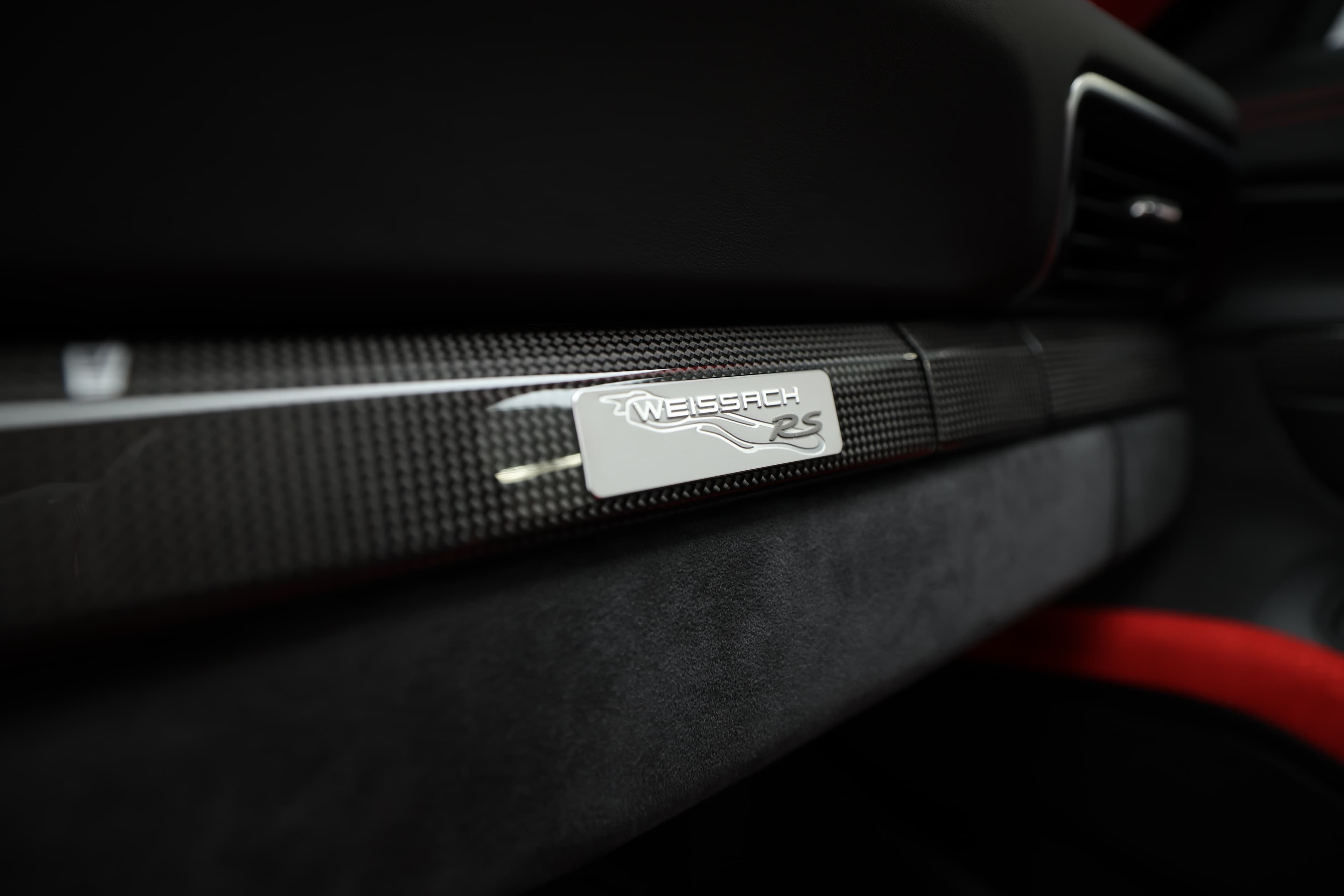 La console centrale côté passager de la Porsche 911 GT2 RS dispose d'un compartiment de rangement, surmonté d'une baguette en carbone avec la plaque 'weissack', ajoutant une touche de sportivité et d'élégance.