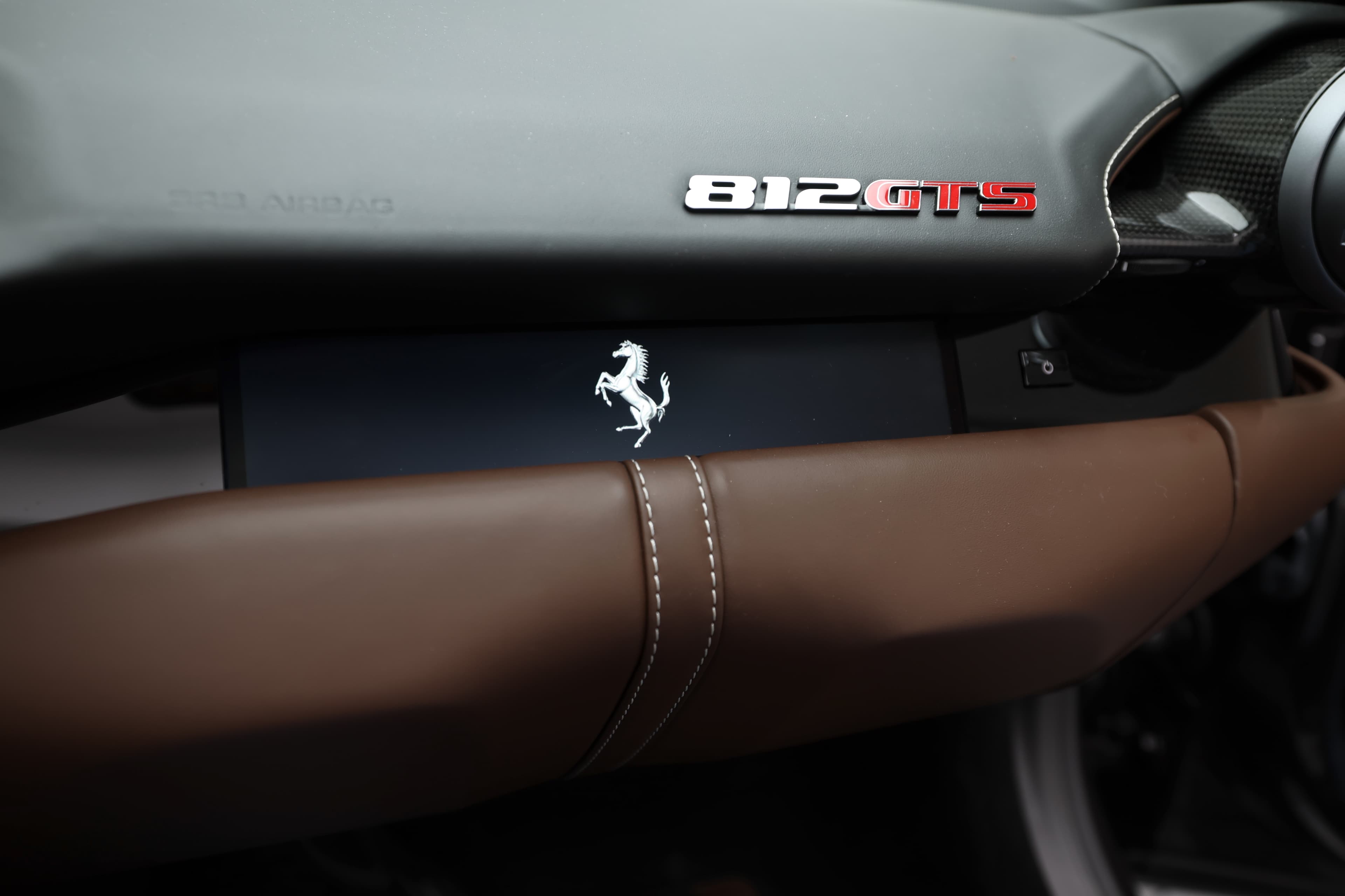 Admirez le tableau de bord de la Ferrari 812 GTS, mettant en avant le badge emblématique et la finition en cuir chocolat. L'harmonie entre les matériaux et les détails raffinés crée une atmosphère de luxe et de sportivité, soulignant l'identité unique de cette supercar.