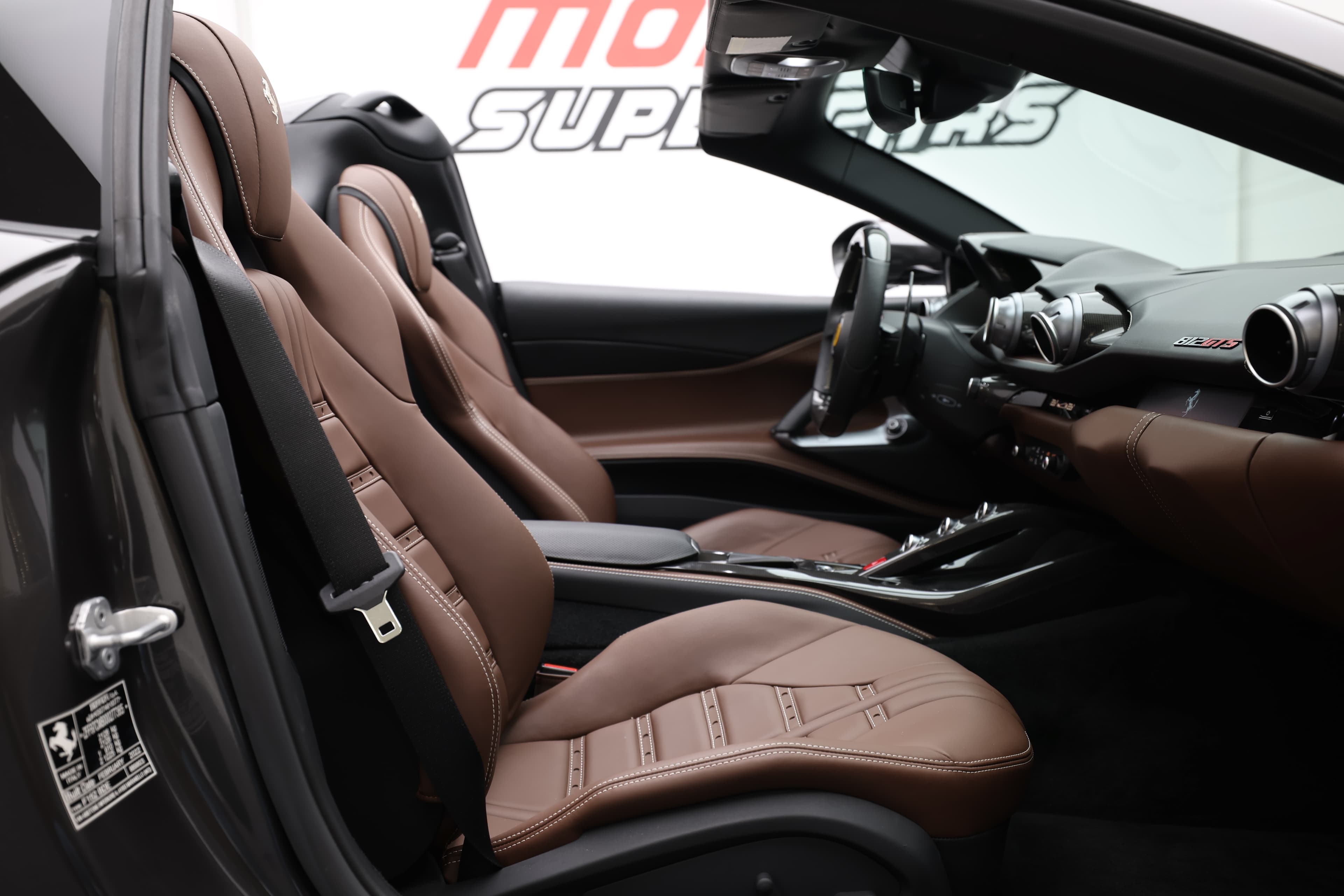 Voici une vue captivante de l'intérieur de la Ferrari 812 GTS, mettant en avant ses sièges en cuir chocolat et son tableau de bord sportif. L'harmonie des matériaux et le design ergonomique créent une atmosphère de luxe et de performance, idéale pour les passionnés de conduite.