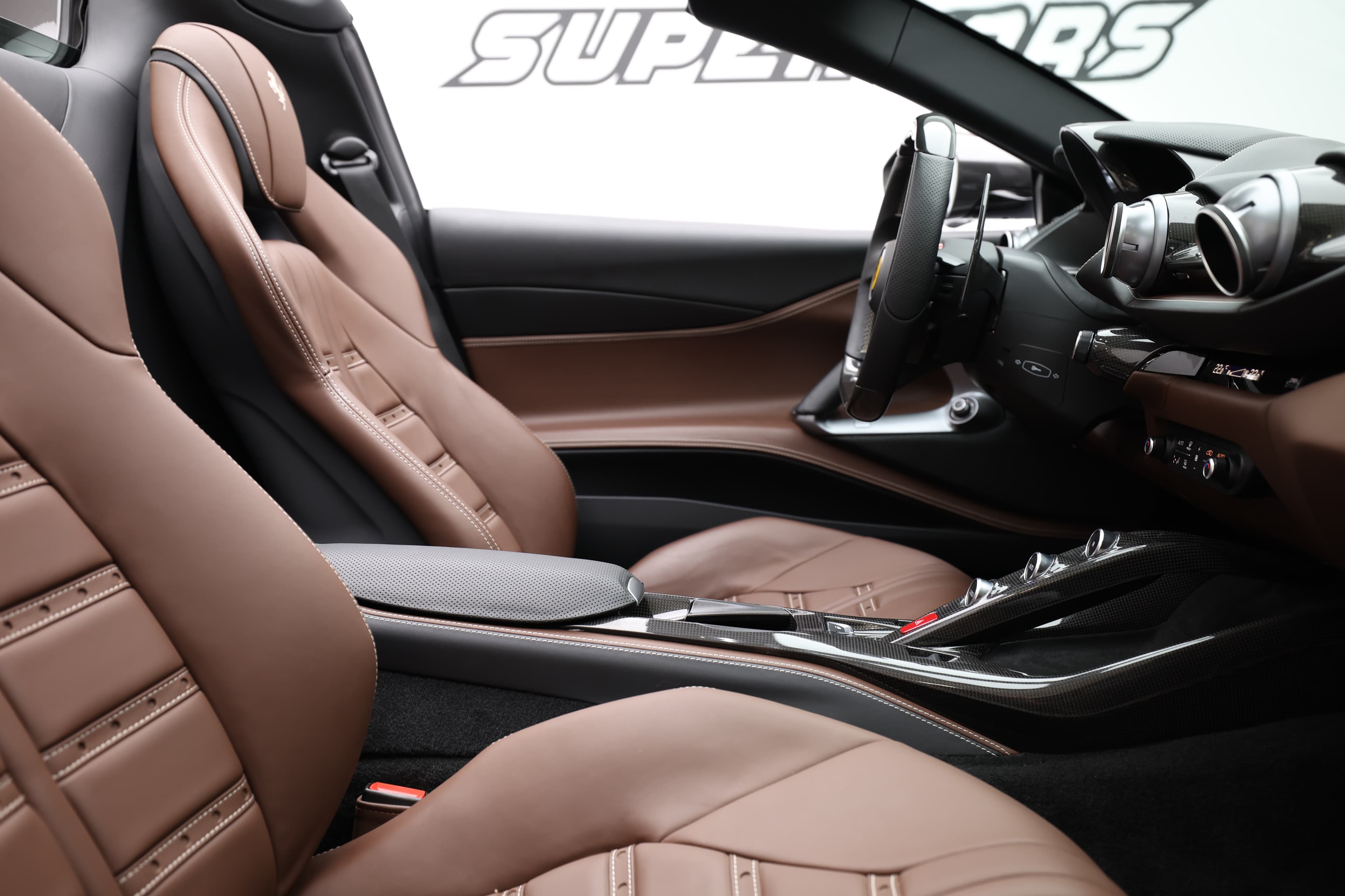 "Voici une autre perspective de l'intérieur de la Ferrari 812 GTS, mettant en avant la combinaison de luxe et de sportivité. Les sièges en cuir chocolat et les finitions en carbone créent une ambiance raffinée, parfaite pour une expérience de conduite inoubliable."