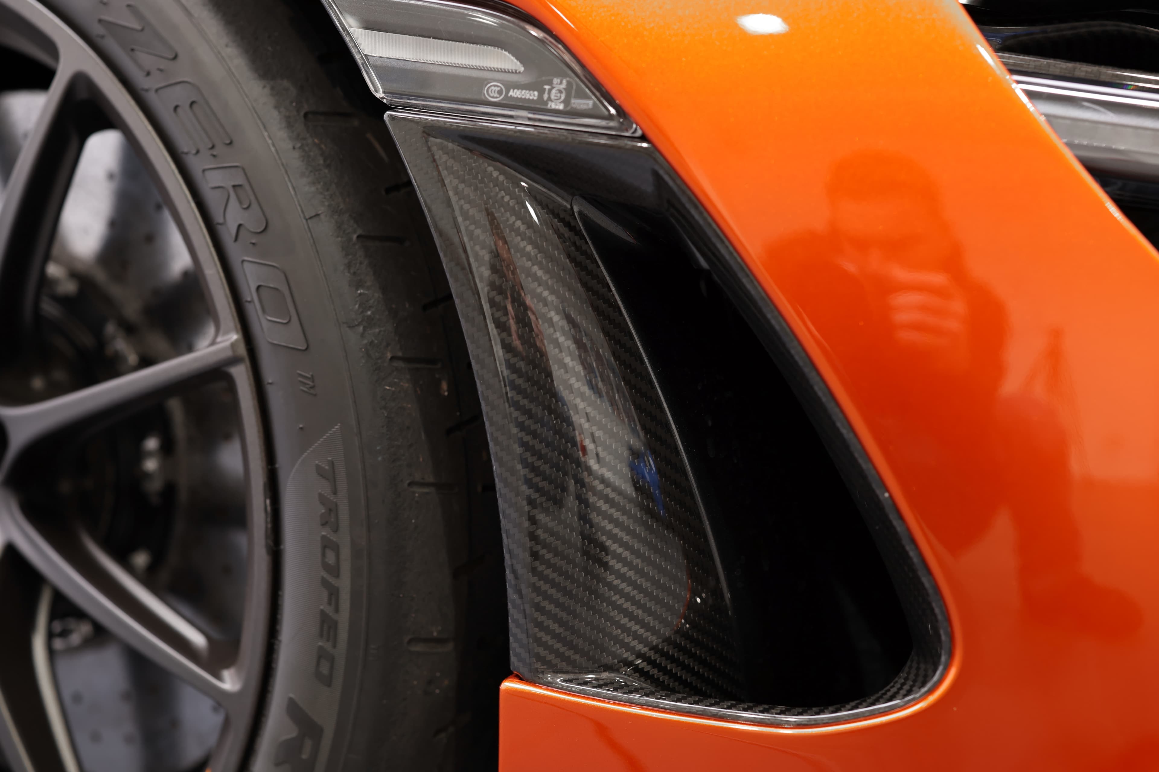 Gros plan sur le détail du passage de roue avant de la McLaren 765LT, mettant en avant l'intégration des éléments en carbone et la conception aérodynamique, soulignant à la fois la performance et le style distinctif de la voiture.