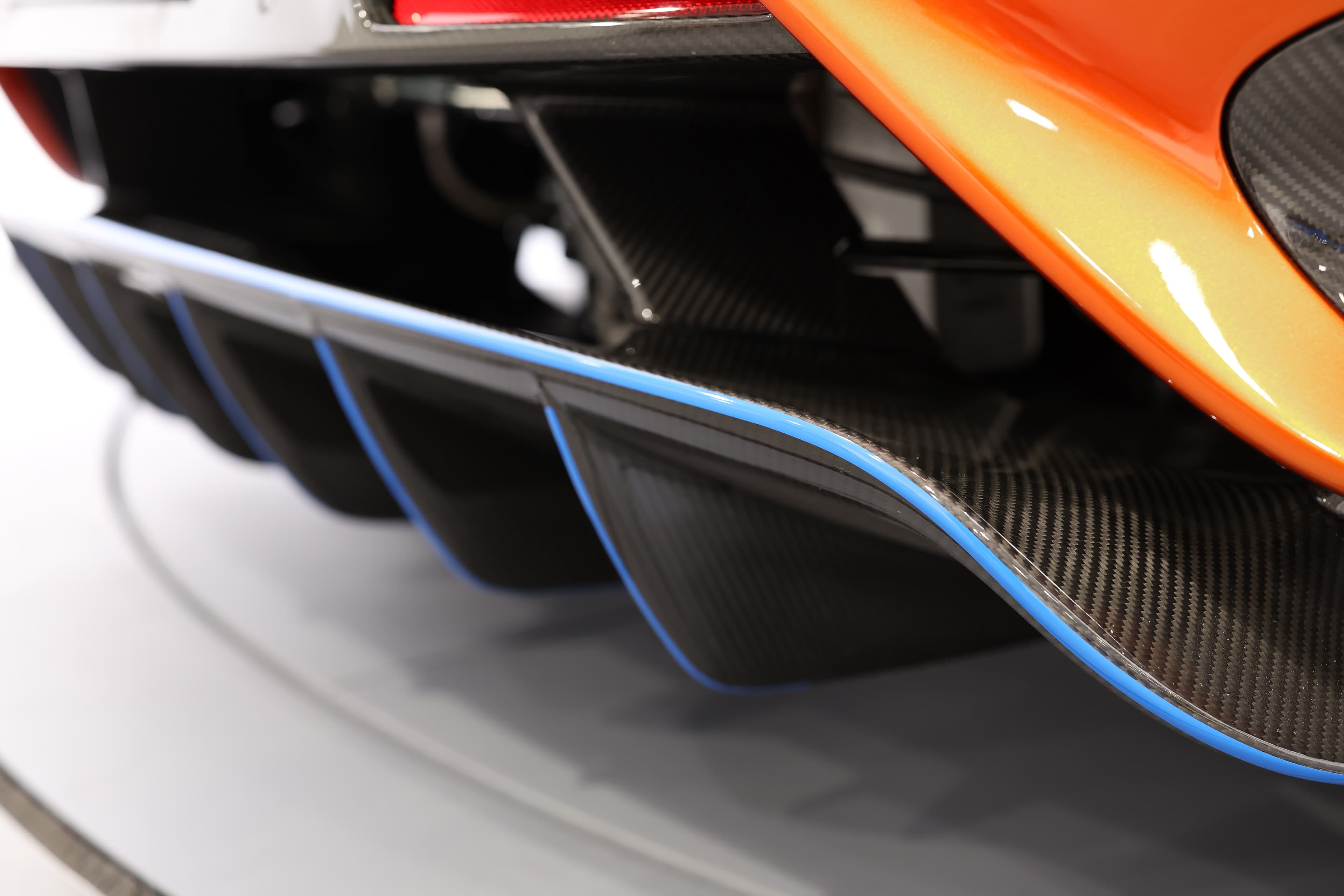 Gros plan sur le diffuseur arrière de la McLaren 765LT, mettant en avant le contraste entre la finition en carbone et les accents bleus, soulignant l'engagement de la marque envers la performance et l'esthétique.