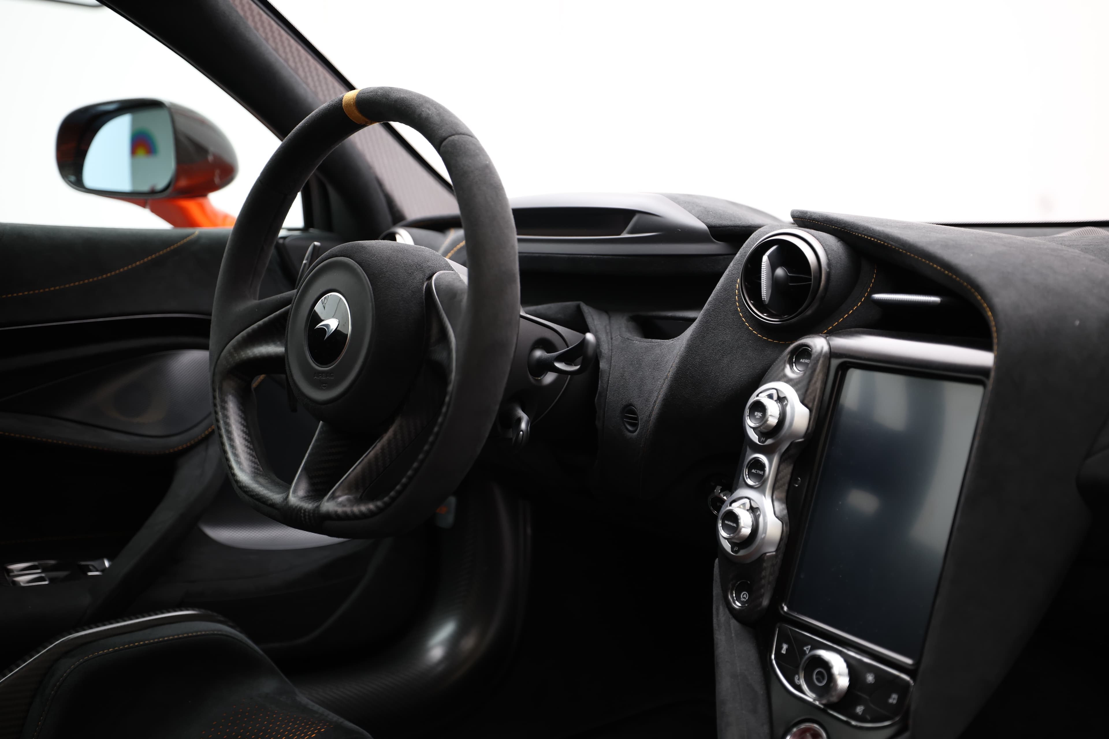 Gros plan sur le tableau de bord et le volant de la McLaren 765LT, montrant les matériaux haut de gamme, l'écran de contrôle et la disposition ergonomique, soulignant l'interface entre conducteur et machine.