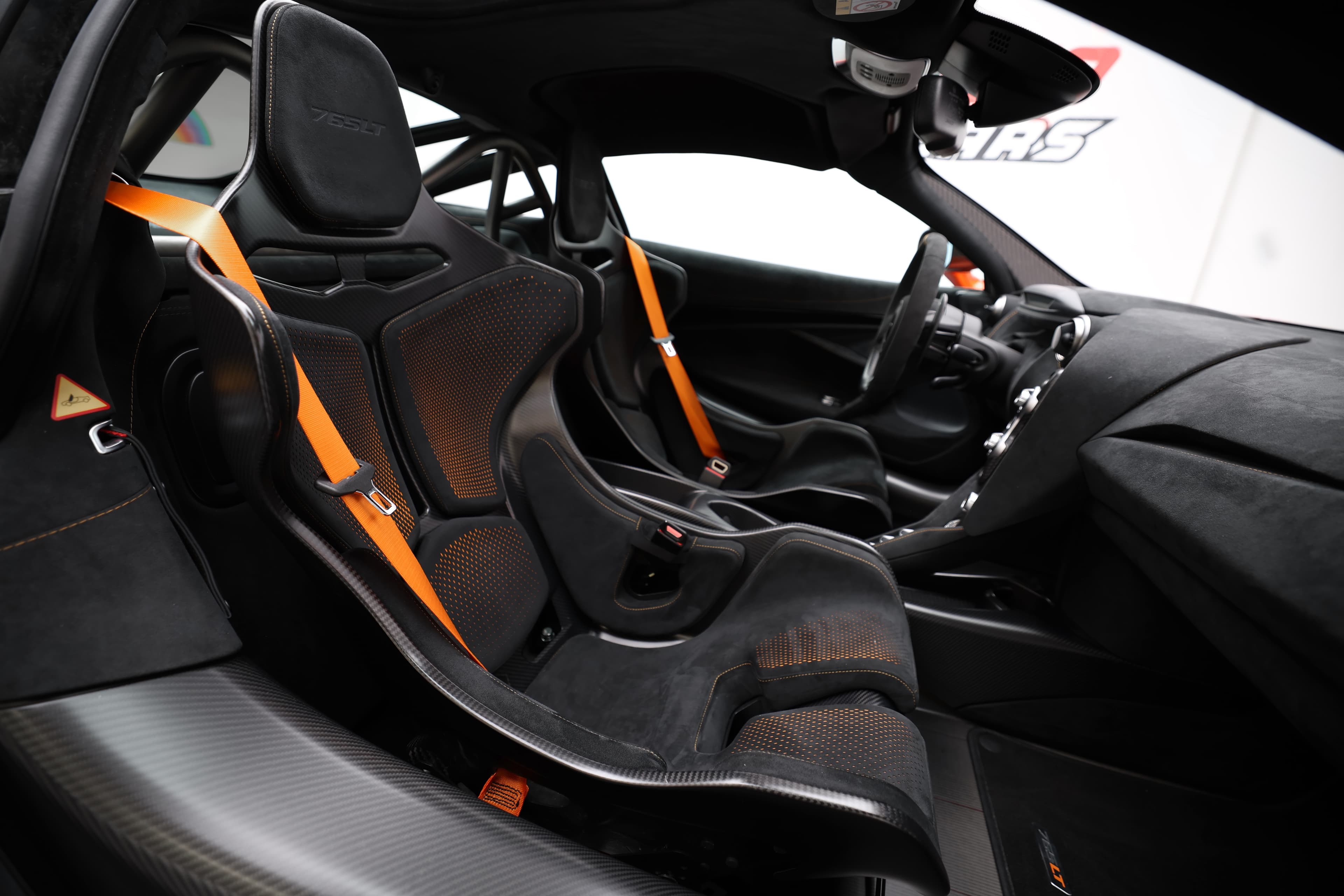 Gros plan sur les sièges en carbone de la McLaren 765LT, mettant en avant les détails de design, les harnais de sécurité et l'intérieur axé sur la performance, illustrant l'engagement envers la course et l'ergonomie.