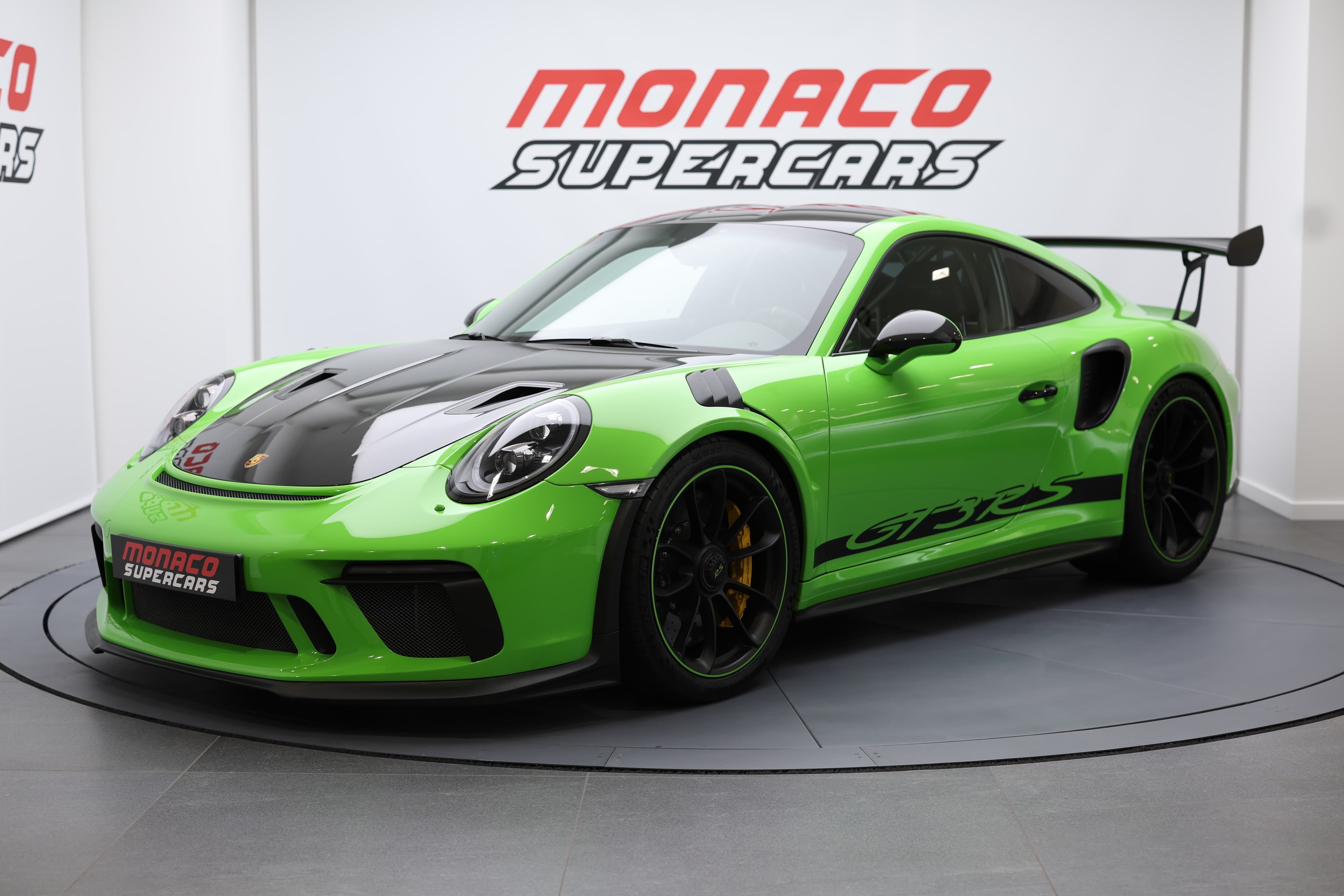 Vue trois-quarts d’une voiture GT3RS verte exposée chez Monaco Supercars, soulignant son aérodynamisme et son caractère ultra-sportif.