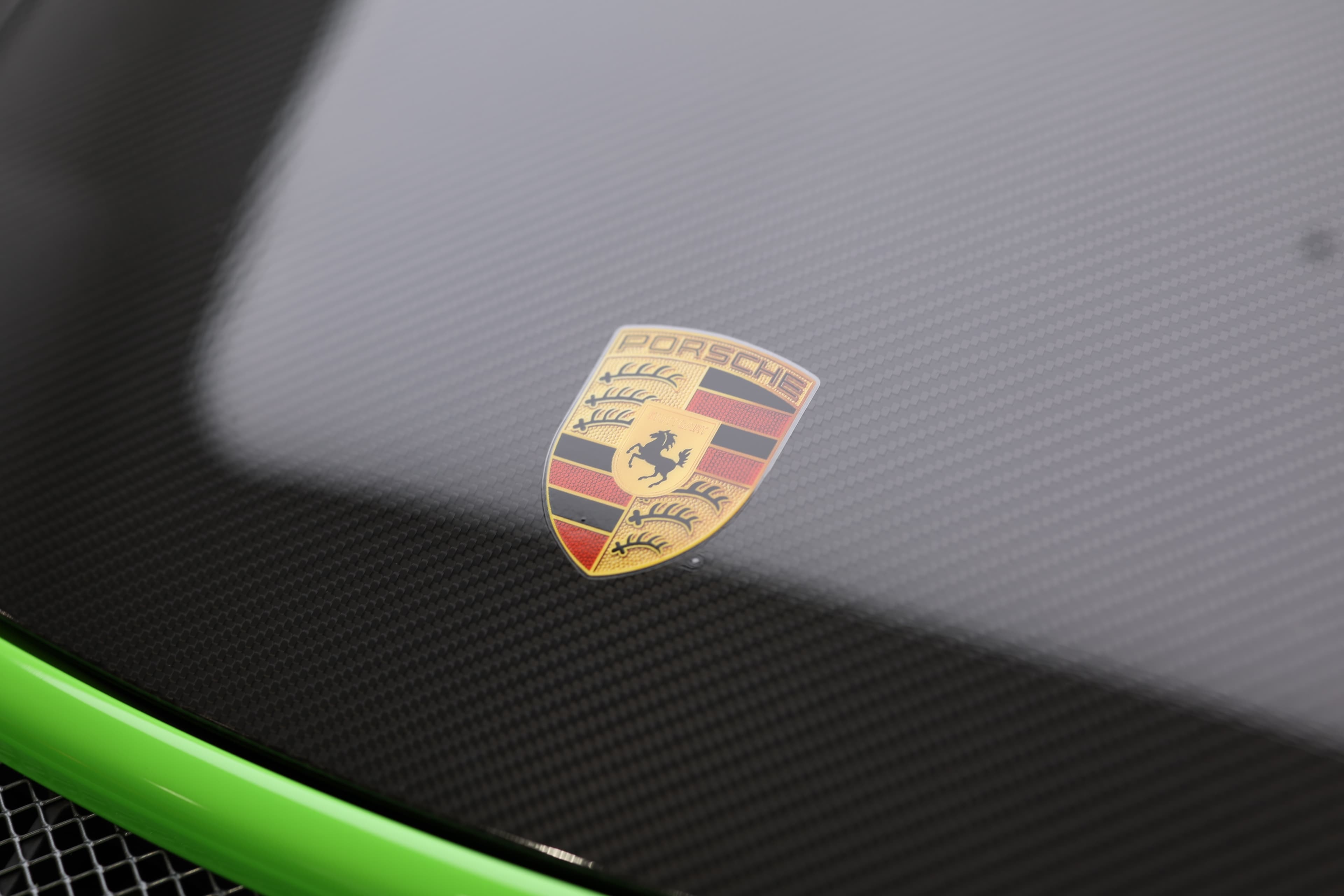 Détail du capot en carbone de la Porsche 911 GT3 RS 991 verte, mettant en valeur l’écusson Porsche et l’utilisation de matériaux légers dédiés à la performance.