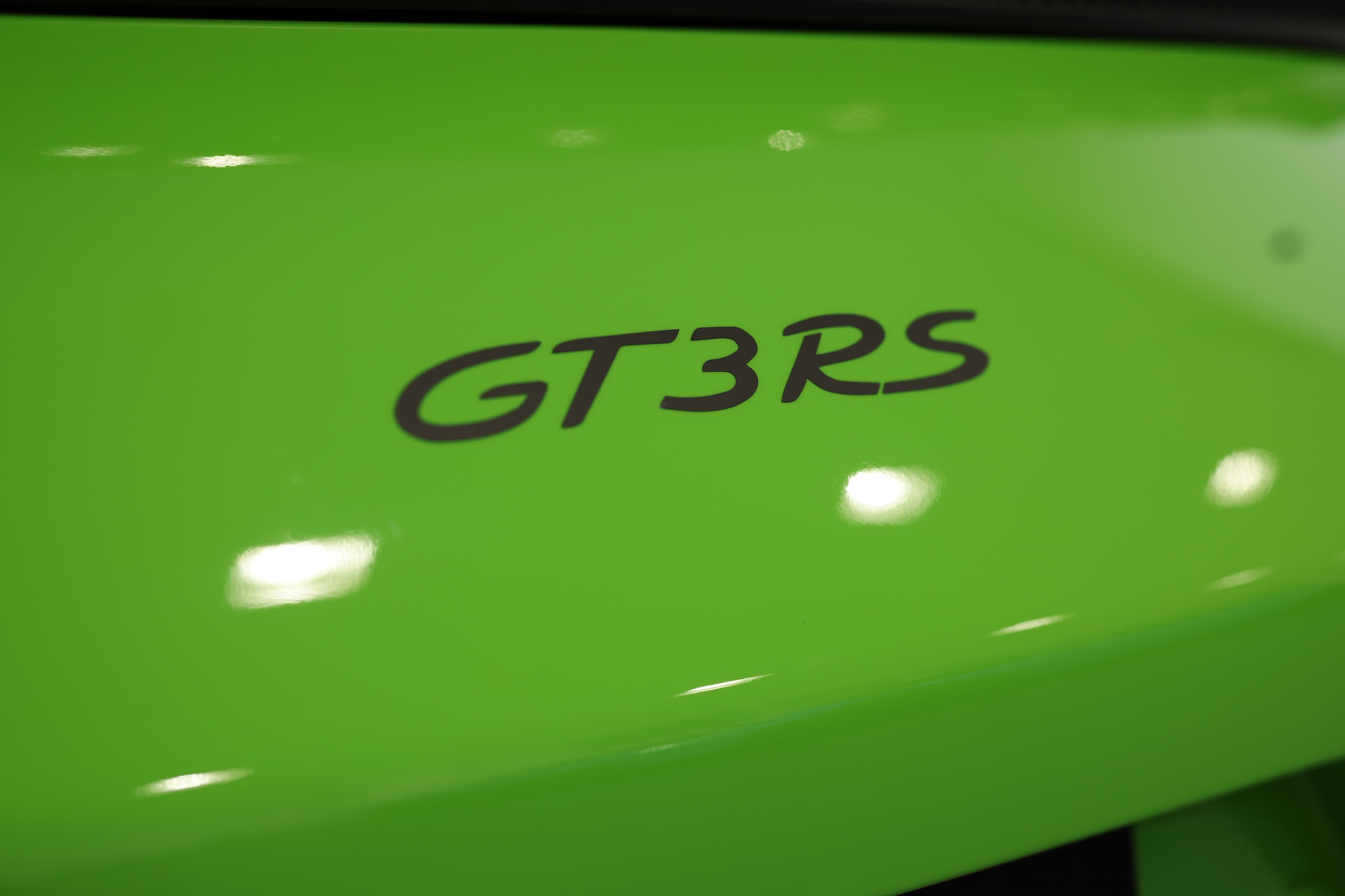 Gros plan sur le badge “GT3 RS” apposé sur la carrosserie vert acide, mettant en valeur la finition peinture et l’identité exclusive du modèle, symbole de la version la plus radicale de la 911 orientée performance et circuit.