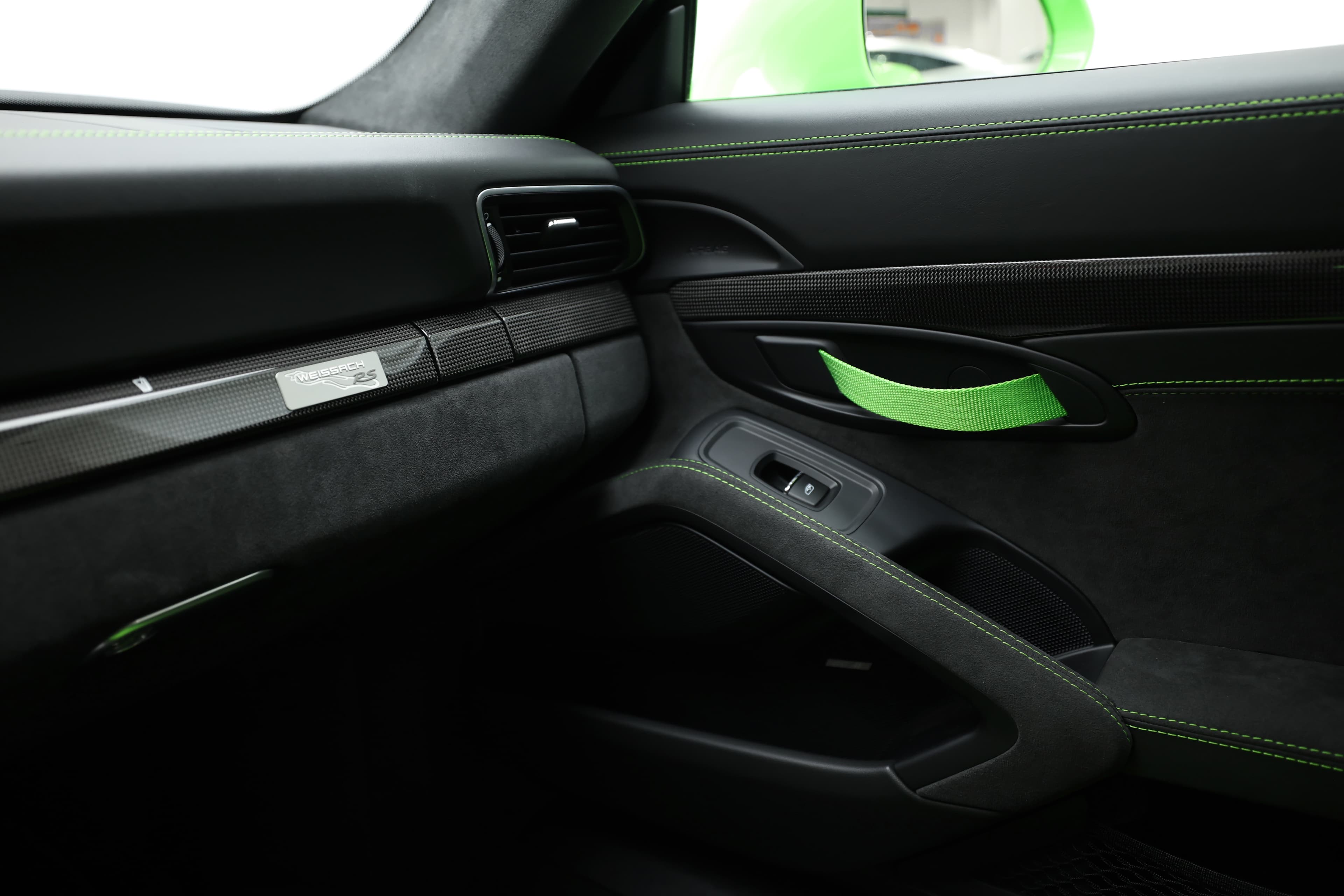 La porte de la Porsche GT3 RS présente des finitions en carbone et en Alcantara, offrant un mélange de luxe et de sportivité. Les accents verts ajoutent une touche dynamique, accentuant l'orientation vers la performance de l'habitacle.