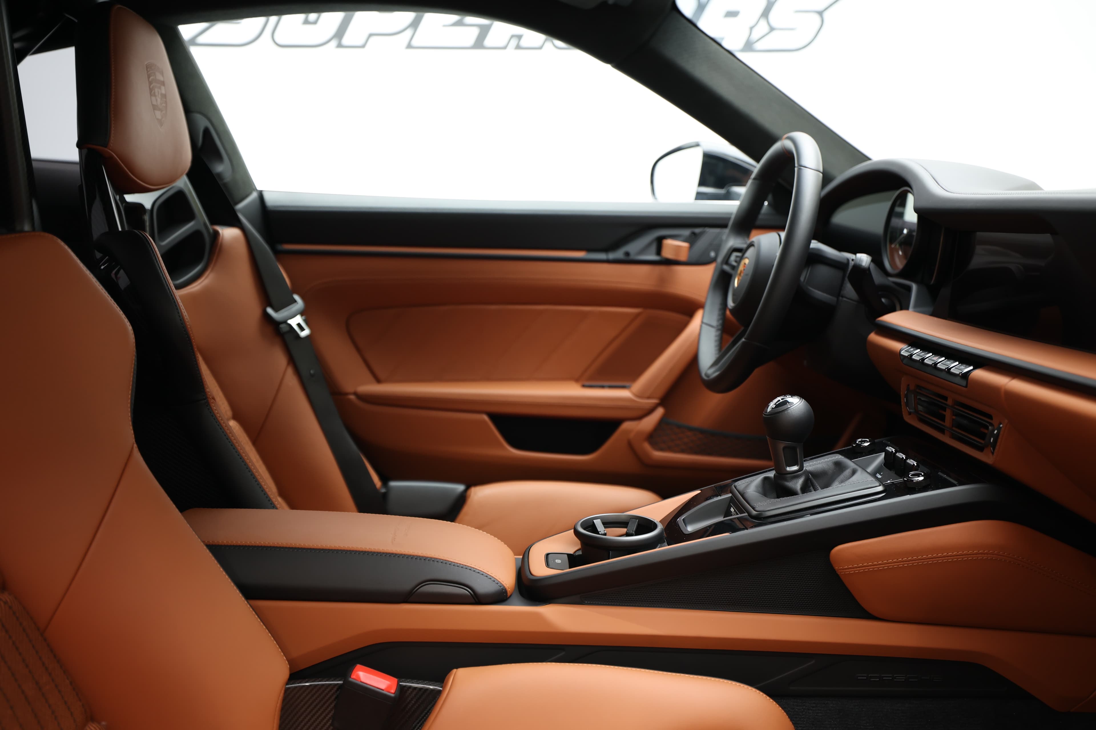 Un intérieur de voiture moderne avec des sièges en cuir orange, un tableau de bord sportif, des éléments en carbone et une technologie avancée, offrant à la fois confort et performance pour une expérience de conduite inégalée.